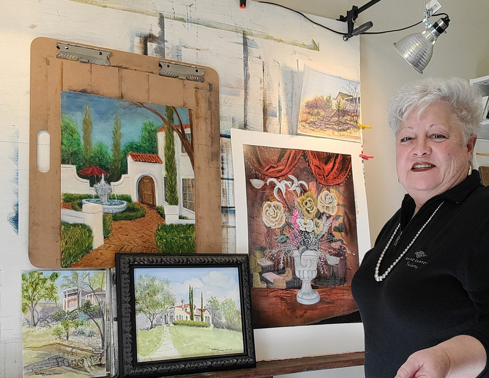 Art easel with several paintings in a variety of mediums that include watercolor, mixed media and oil painting techniques.